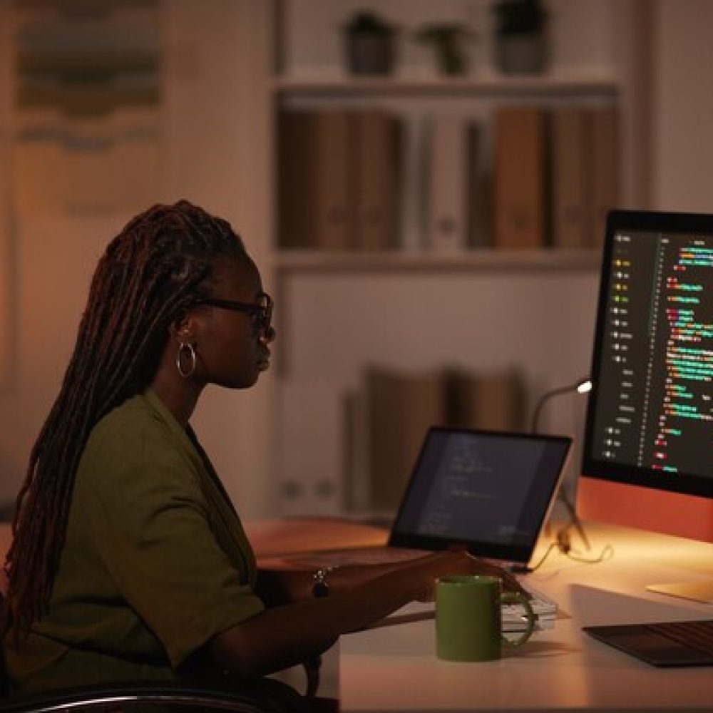 side-view-portrait-contemporary-african-american-woman-writing-code-looking-computer-screen-while-working-dim-office-copy-space_236854-25125